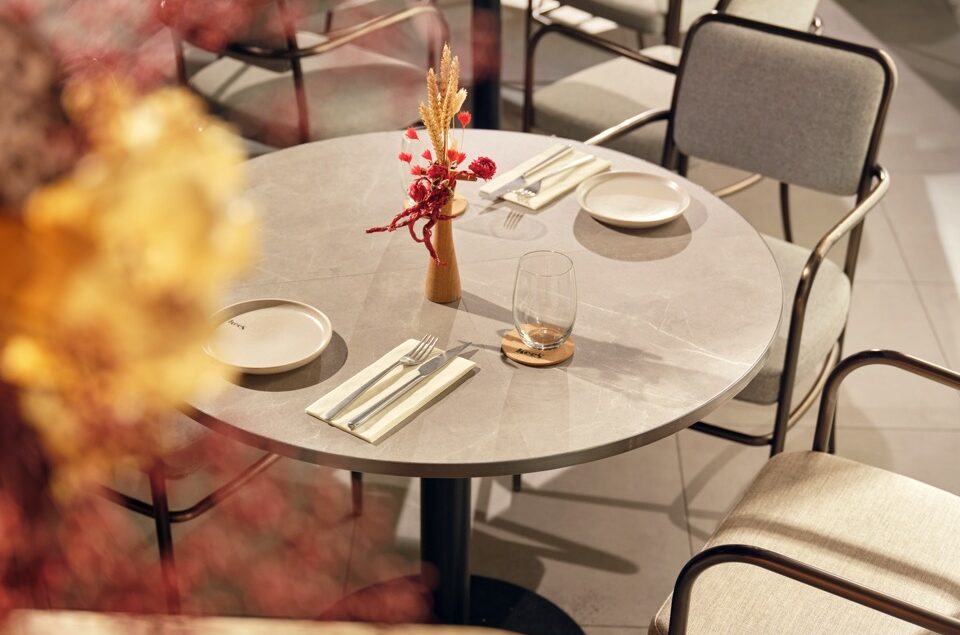 Sunlit dining area at Kee’s restaurant in 21 Carpenter Singapore, featuring round marble tables, upholstered chairs, floral centrepieces and contemporary interiors.